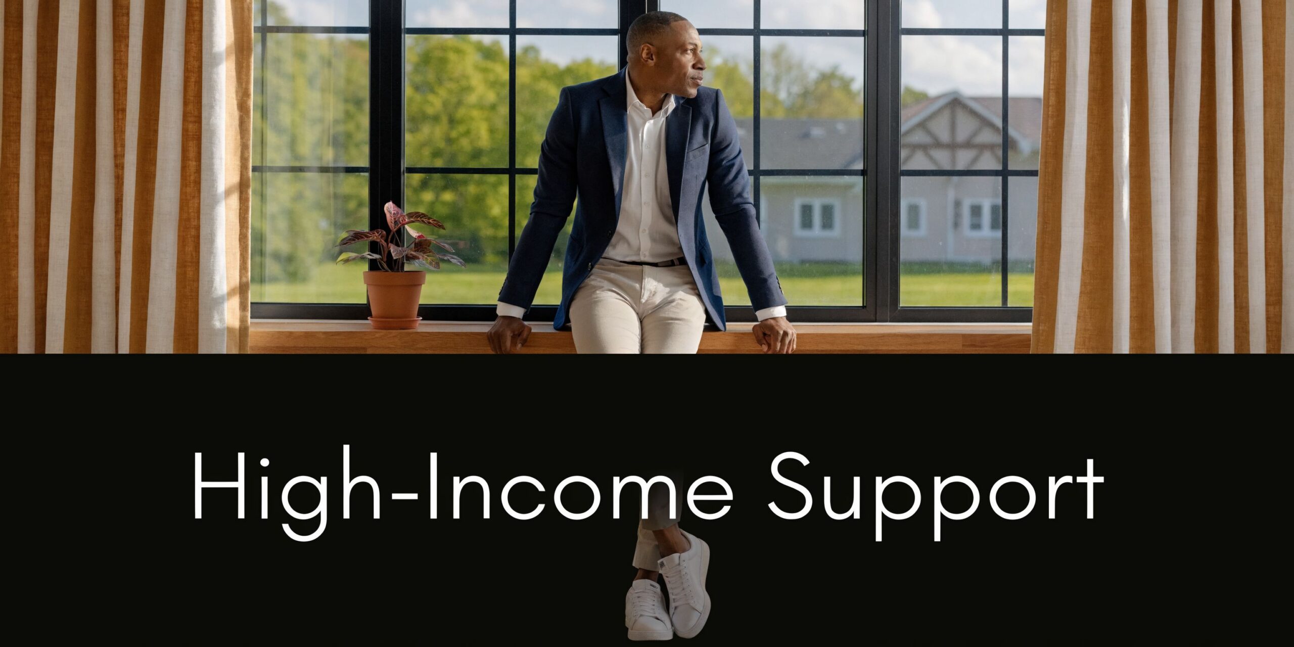 A professional man sitting on a window sill looking out at a suburban house and garden.