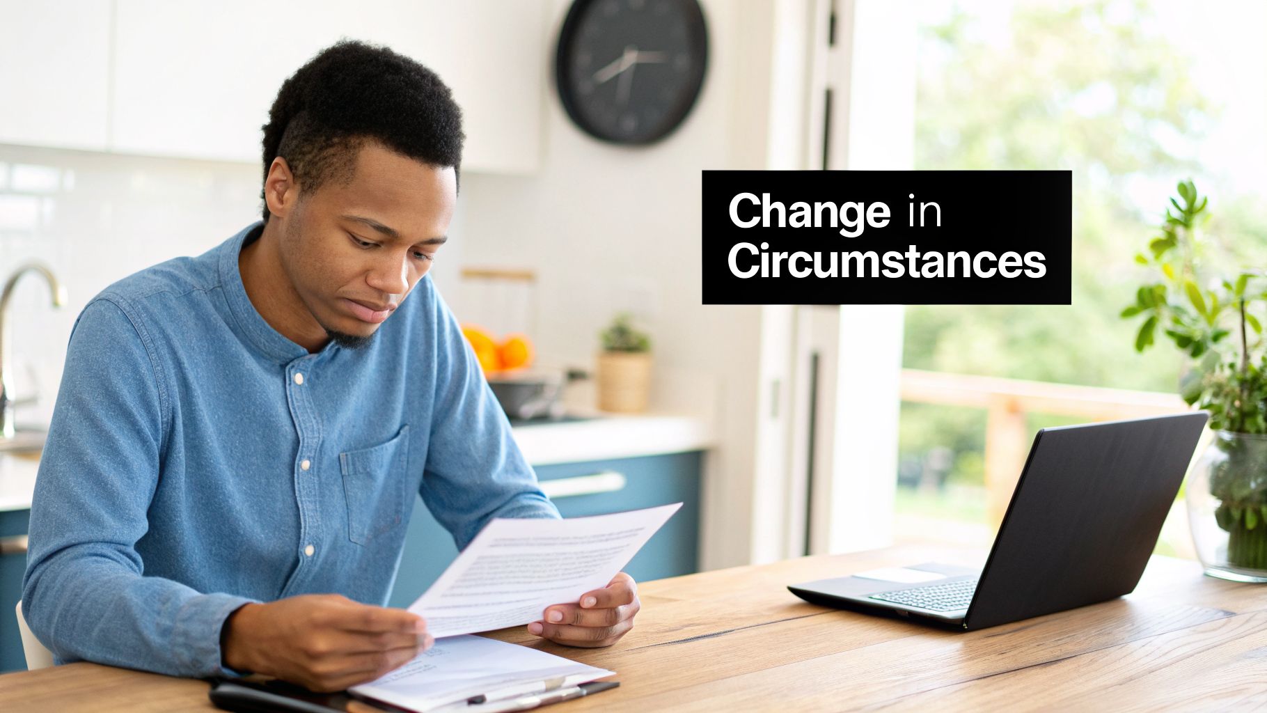 Young man seriously reviewing documents at a table with a laptop, facing a 'Change in Circumstances'.