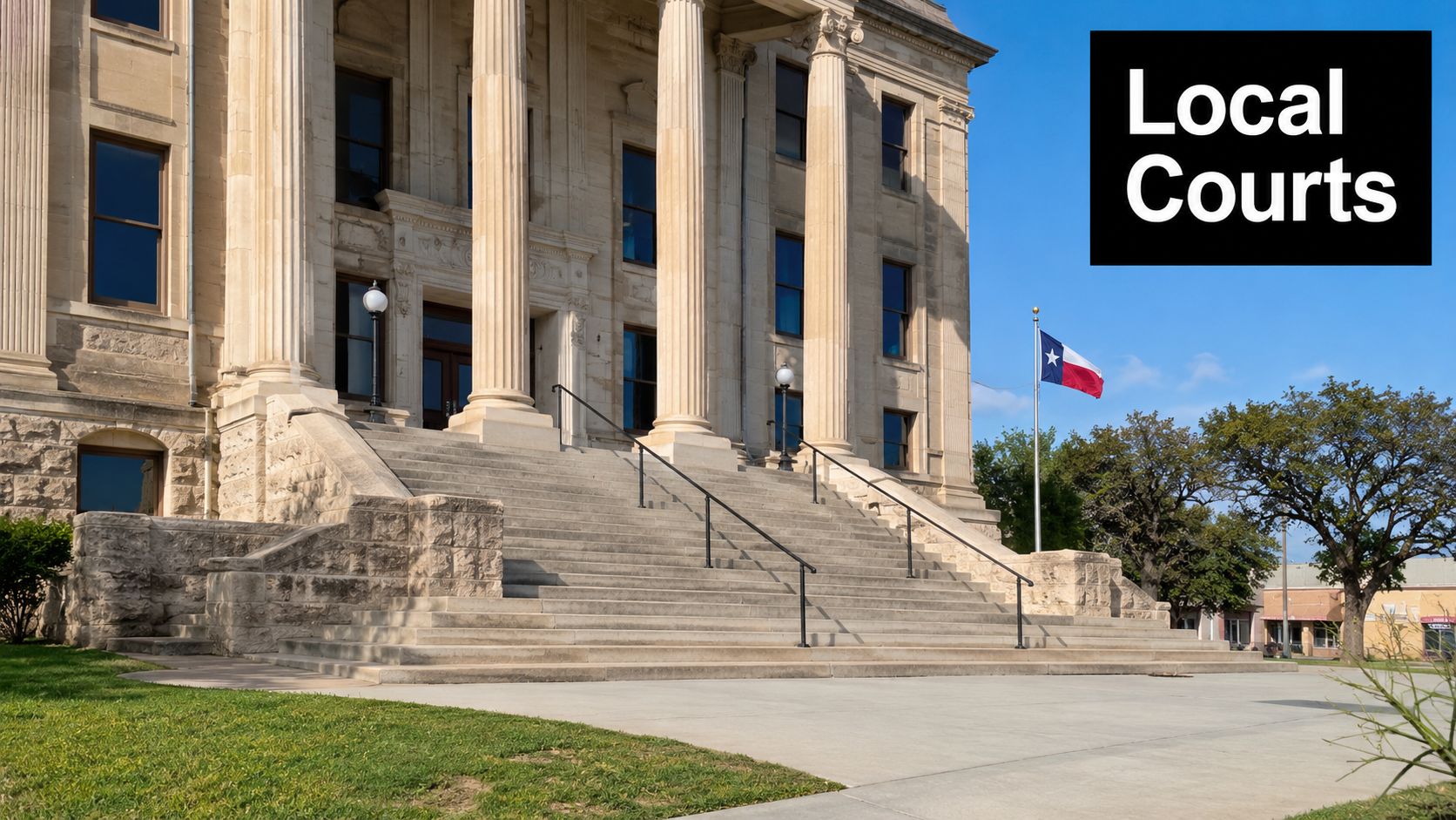 A historic Texas courthouse building featuring grand stone columns, wide steps, and the Texas state flag flying.